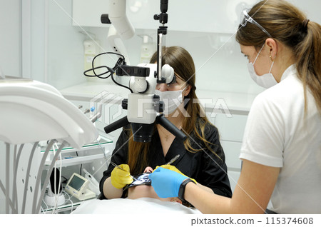 cofferdam clamp for cofferdam The process of dental prosthetics using a microscope, female doctor in yellow gloves, patient dentist with patient, using dental curing light 115374608