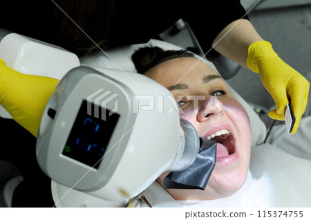 latest technology in dental clinic new x-ray scanner woman is taken picture after filling canals woman smiles pretty doctor yellow gloves special device for photography jaws of teeth and gums x-ray latest technology in dental clinic new x-ray scanner woman is taken picture after filling canals woman smiles pretty doctor yellow gloves special device for photography jaws of teeth and gums x-ray 115374755