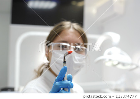 woman doctor holding a tooth covered in blood in front of her face Dentist has extracted a sick tooth from patient in dental office dental tongs or pliers and extracted lower tooth in it. Dentistry 115374777
