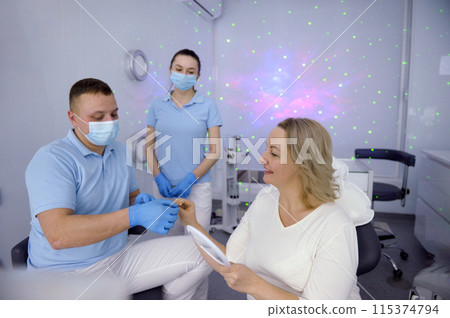 dental clinic patient reception in lilac hall with stars intimate atmosphere doctor and nurse in masks wearing blue gloves offer women color options teeth whitening latest technology 115374794