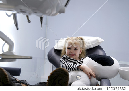 beautiful little blond blonde girl in dentist office big shoes on feet close-up latest technology soft toy in hands smile meeting the doctor alone in the frame slow slow motion camera zooms in and out beautiful little blond blonde girl in dentist office big shoes on feet close-up latest technology soft toy in hands smile meeting the doctor alone in the frame slow slow motion camera zooms in and out 115374882