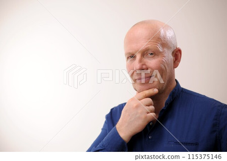 approve it Emotions of an adult handsome bald man A man on a white background in a blue shirt The man likes the situation, he touches his chin with his hand and grins a little, his eyes sparkle and approve it Emotions of an adult handsome bald man A man on a white background in a blue shirt The man likes the situation, he touches his chin with his hand and grins a little, his eyes sparkle and 115375146