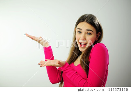 Thoughtful woman Show hands on empty space advertising looks pensively above dressed in casual pink jumper poses against blank copy space for your advertising content thinks about future 115375156
