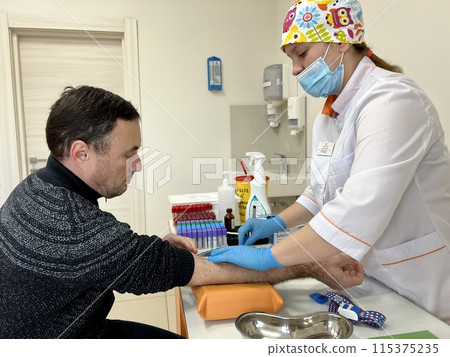 Close up of nurse disinfecting male arm before blood test. Man is sitting on chair near medical set Skillful general practitioner testing male blood Close up of nurse disinfecting male arm before blood test. Man is sitting on chair near medical set Skillful general practitioner testing male blood 115375235