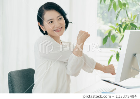 A woman stretching in front of a computer A woman stretching in front of a computer 115375494