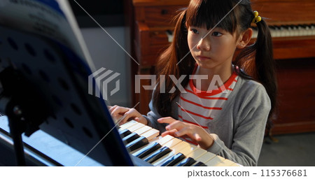 An Asian girl with black hair plays the piano, concentrating on the music sheets An Asian girl with black hair plays the piano, concentrating on the music sheets 115376681