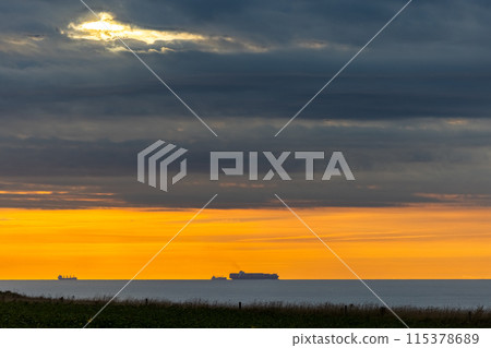 The ocean at sunset was calm, with ships on the horizon and a peaceful atmosphere 115378689