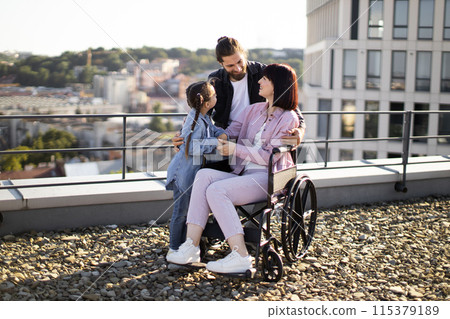 Young woman in wheelchair having fun with family on terrace of modern house. 115379189