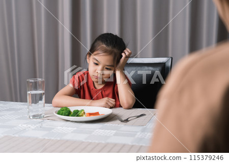 Mother is telling her cute kid eat useful vegetables but the child refuses to eat. 115379246