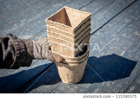 Peat pots in stack for seedlings in hand with gloves, spring gardening Peat pots in stack for seedlings in hand with gloves, spring gardening 115380375