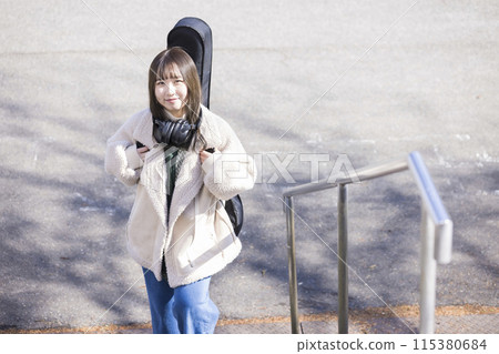 A young woman carrying a guitar case going up the stairs 115380684