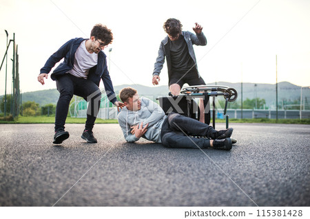 Young disabled man fall off wheelchair, fiends helping to sit back. Male friendship. 115381428