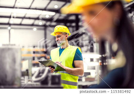 Warehouse employees in warehouse. Two workers in reflective clothing in modern industrial factory, heavy industry, manufactrury. 115381492