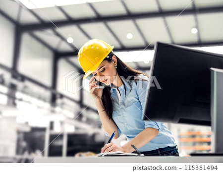 Female project manager standing in modern industrial factory, making phone call. Manufacturing facility with robotics, robotic arms and automation. Storing products and materials in warehouse. Female project manager standing in modern industrial factory, making phone call. Manufacturing facility with robotics, robotic arms and automation. Storing products and materials in warehouse. 115381494