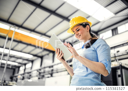 Female project manager standing in modern industrial factory. Manufacturing facility with robotics, robotic arms and automation. Storing products and materials in warehouse. 115381527