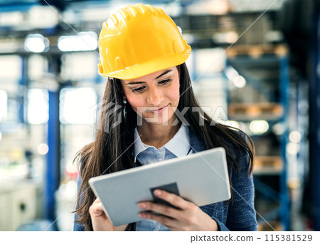 Female project manager standing in modern industrial factory. Manufacturing facility with robotics, robotic arms and automation. Storing products and materials in warehouse. 115381529