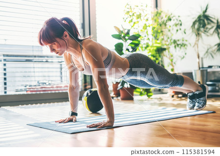 Beautiful redhead woman's home fitness routine. Home workout on gym mt in living room, sporty woman wearing sportswear. Beautiful redhead woman's home fitness routine. Home workout on gym mt in living room, sporty woman wearing sportswear. 115381594