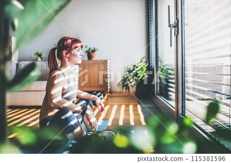 Beautiful redhead woman's home fitness routine. Home workout on gym mt in living room, sporty woman wearing sportswear. 115381596