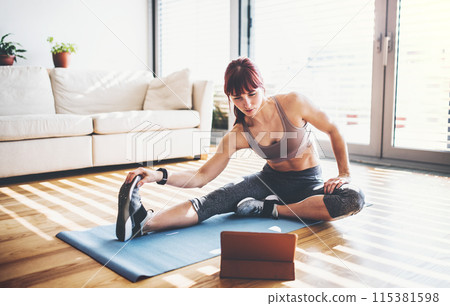 Beautiful redhead woman's home fitness routine. Home workout on gym mt in living room, sporty woman wearing sportswear. 115381598