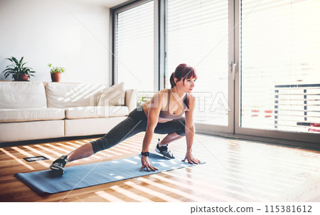 Beautiful redhead woman's home fitness routine. Home workout on gym mt in living room, sporty woman wearing sportswear. 115381612