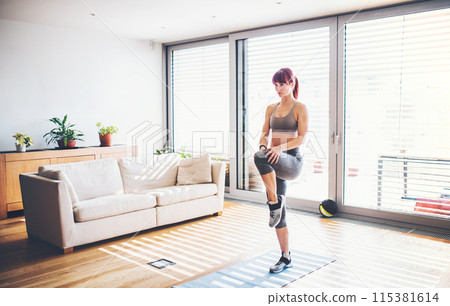 Beautiful redhead woman's home fitness routine. Home workout on gym mt in living room, sporty woman wearing sportswear. 115381614