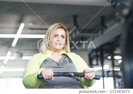 Overweight woman exercising on rowing machine. Routine workout for physical and mental health 115381673
