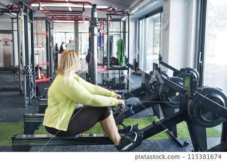 Overweight woman exercising on rowing machine. Routine workout for physical and mental health 115381674