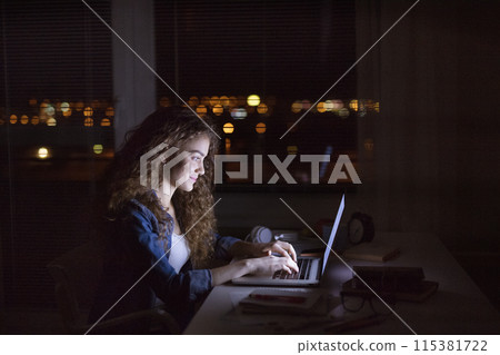 Beautiful university student is writing her thesis on a laptop at night, sitting at home at table, focusing on her research. Preparing for final exam, studying. Beautiful university student is writing her thesis on a laptop at night, sitting at home at table, focusing on her research. Preparing for final exam, studying. 115381722