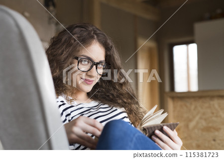 Female student sitting in armchair, reading book, studying for final exam at university. Beautiful woman relaxing at home. Female student sitting in armchair, reading book, studying for final exam at university. Beautiful woman relaxing at home. 115381723