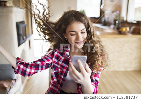 University student sitting at home on the floor scrolling on smartphone. 115381737