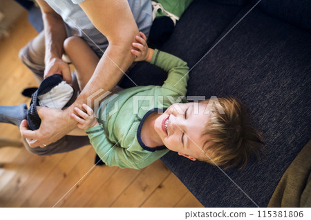 Father trying to put clothes on his toddler son, laughing. Hard work. Father trying to put clothes on his toddler son, laughing. Hard work. 115381806