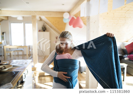 Mother holding small baby, putting her in baby sling, wrap. Unconditional paternal love, mother's Day. 115381860