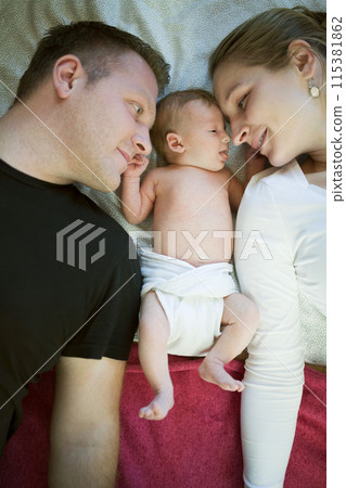 New parents lying on bed by newborn baby girl. Unconditional paternal love, idyllic family moment. 115381862