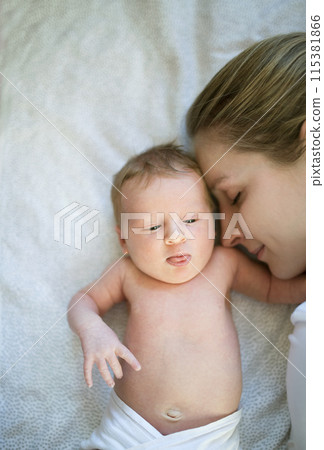 New mom lying on bed by newborn baby girl. Unconditional paternal love, idyllic family moment. New mom lying on bed by newborn baby girl. Unconditional paternal love, idyllic family moment. 115381866
