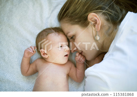 New mom lying on bed by newborn baby girl. Unconditional paternal love, idyllic family moment. New mom lying on bed by newborn baby girl. Unconditional paternal love, idyllic family moment. 115381868