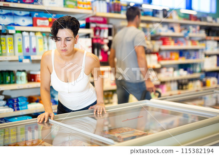 Woman standing at refrigerator in supermarket, choosing frozen food 115382194