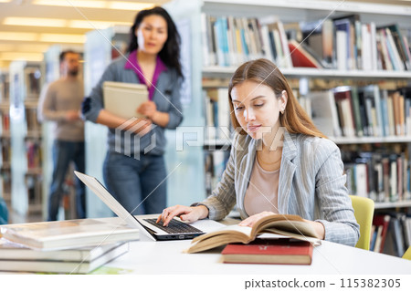 Young woman working with books and laptop on project in library Young woman working with books and laptop on project in library 115382305