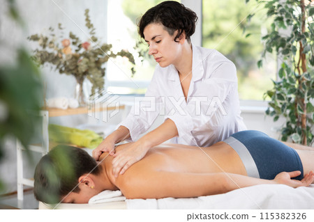 Diligent woman massage therapist massaging relaxing guy at spa complex 115382326