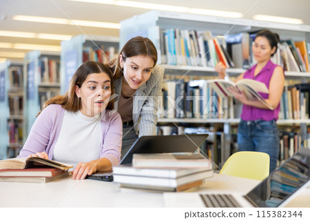 Two female students studying in library with books and laptop Two female students studying in library with books and laptop 115382344