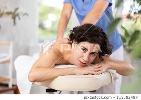 Portrait of woman enjoying relaxing massage by professional masseur 115382497