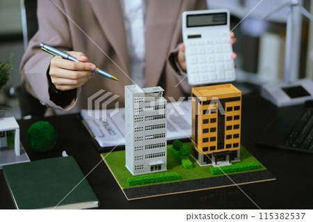 home loan officer uses a calculator with a house plan on a wooden table.. home loan officer uses a calculator with a house plan on a wooden table.. 115382537