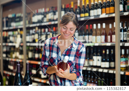 Positive woman choosing wine in supermarket Positive woman choosing wine in supermarket 115382817