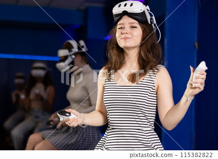 Cheerful teen girl sitting in virtual reality gaming lounge Cheerful teen girl sitting in virtual reality gaming lounge 115382822