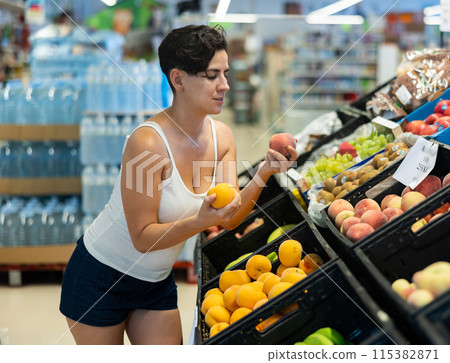 Portrait of cheerful female buyer taking fresh ripe peaches on supermarket 115382871