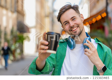 Happy smiling man enjoying morning coffee hot drink relaxing, taking a break walking on city street Happy smiling man enjoying morning coffee hot drink relaxing, taking a break walking on city street 115383465