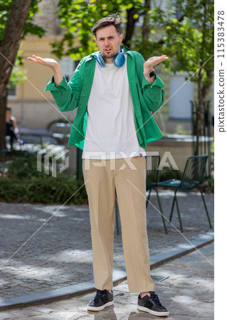 Confused young man feeling embarrassed about ambiguous question having doubts no idea outdoors Confused young man feeling embarrassed about ambiguous question having doubts no idea outdoors 115383478