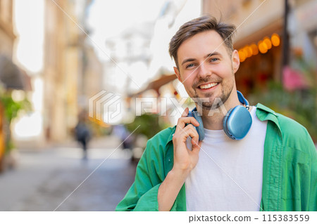 Portrait of smiling young male tourist in casual clothes with wireless headphones around neck 115383559