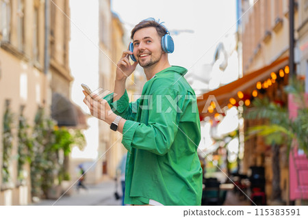 Rear view of happy relaxed man tourist in wireless headphones listening music walking on city street 115383591