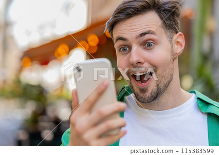 Excited happy winner man using smartphone looking amazed at screen celebrating win good message news Excited happy winner man using smartphone looking amazed at screen celebrating win good message news 115383599