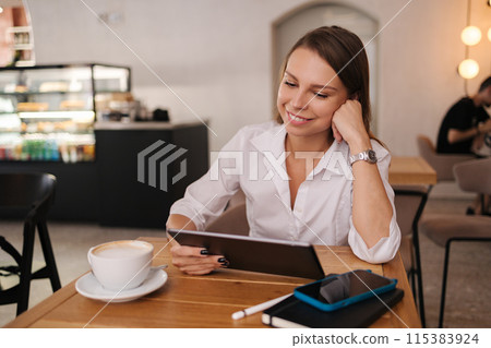 Female freelancer working in cafe using digital tablet. Young business manager drink coffee during work break Female freelancer working in cafe using digital tablet. Young business manager drink coffee during work break 115383924